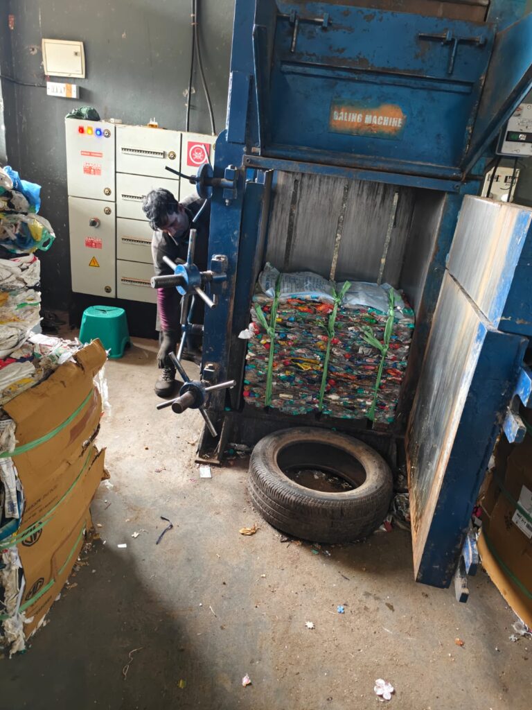 A worker operating a baling machine to compress segregated dry waste into bales at an EcoGram recycling facility in North Bengaluru.